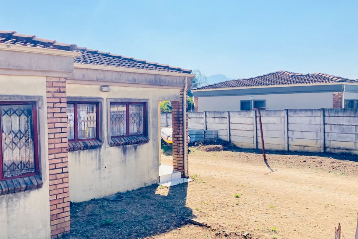 Rear view of the property featuring a tiled roof, security bars on windows, and a precast concrete boundary wall enclosing the unpaved yard area.