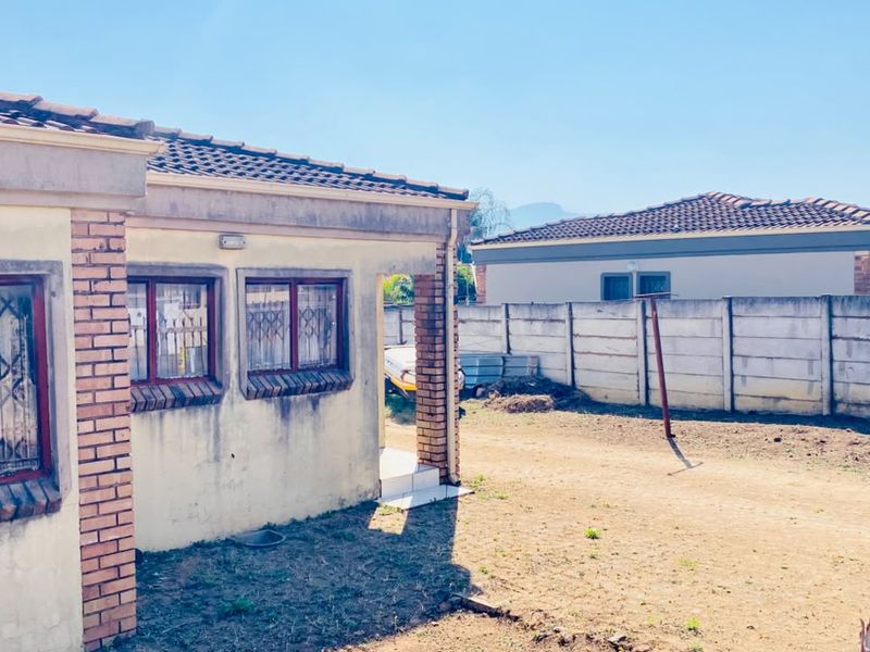 Rear view of the property featuring a tiled roof, security bars on windows, and a precast concrete boundary wall enclosing the unpaved yard area.