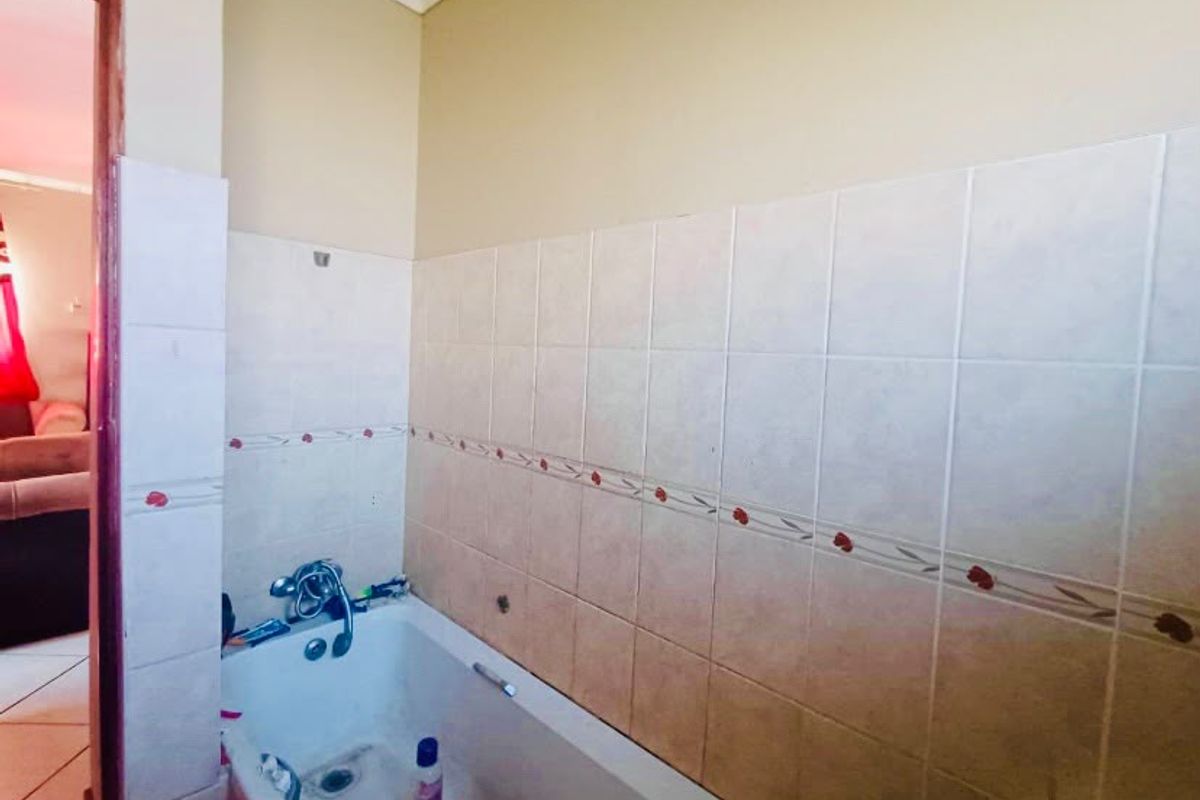 A functional bathroom featuring a built-in bathtub with wall tiling, requiring some cosmetic updates to improve the overall aesthetic and finish.