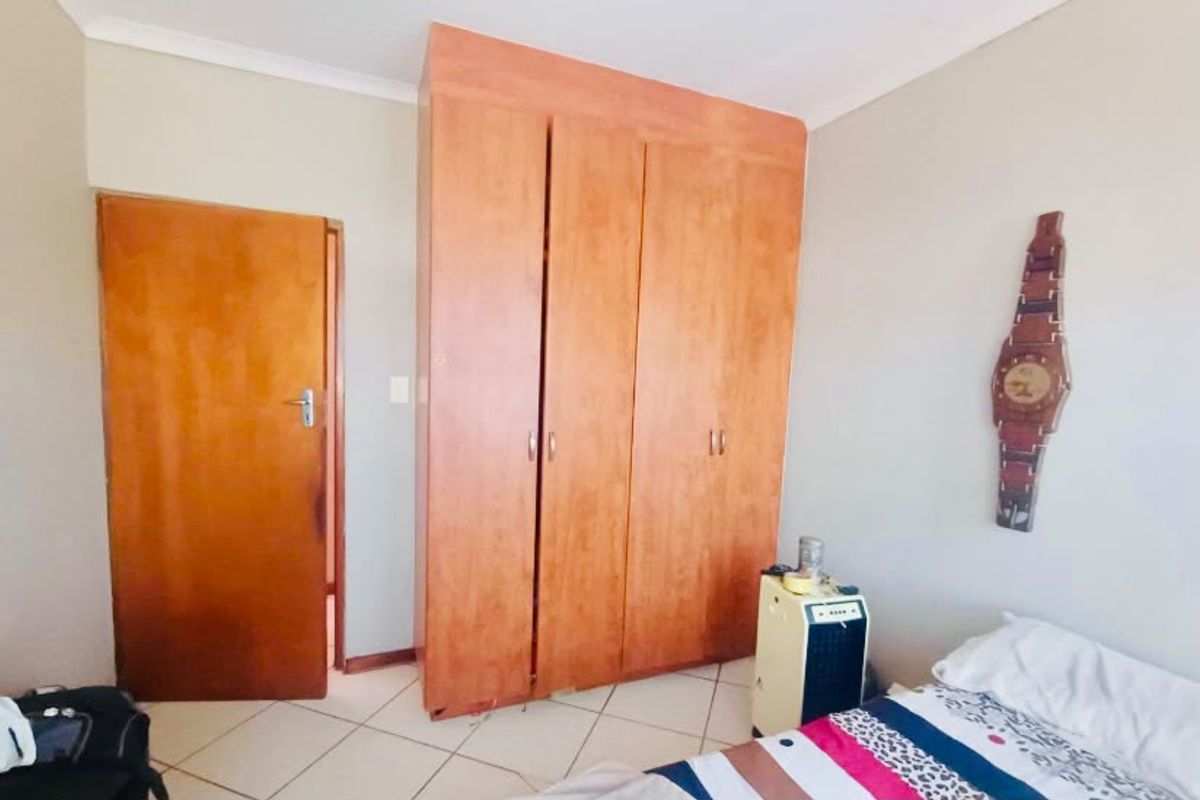 A bedroom featuring built-in wooden cupboards, tiled flooring, and neutral wall finishes.