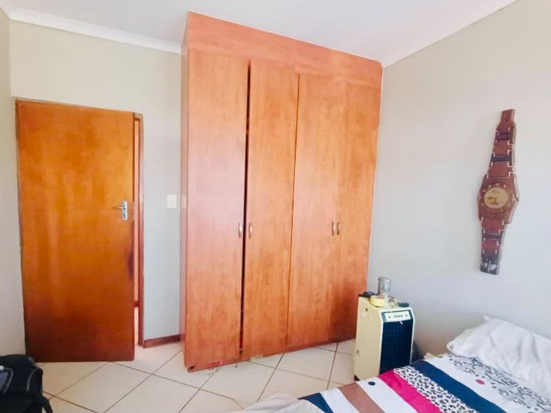 A bedroom featuring built-in wooden cupboards, tiled flooring, and neutral wall finishes.