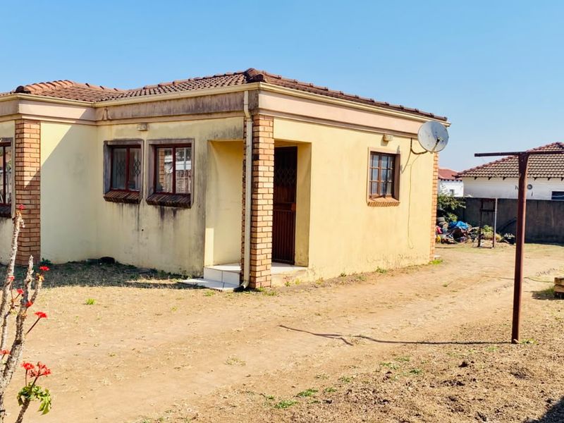 Rear view of a single-story detached house featuring a tiled roof, brick accents, and exterior walls showing signs of weathering and staining.