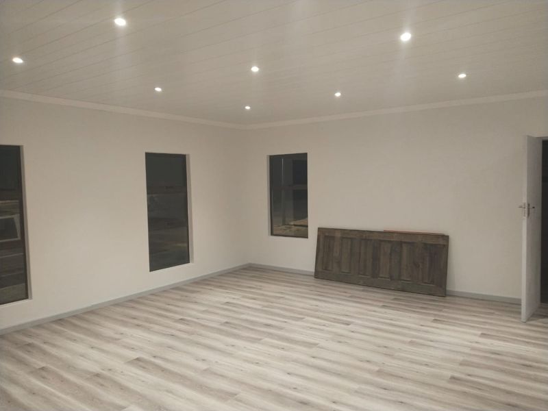 A bright, empty living area featuring modern laminate flooring, recessed downlighting, and a clean, neutral aesthetic ready for furnishing.