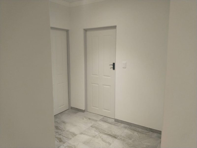 A clean, neutral hallway featuring modern grey-toned tiled flooring and white internal doors.