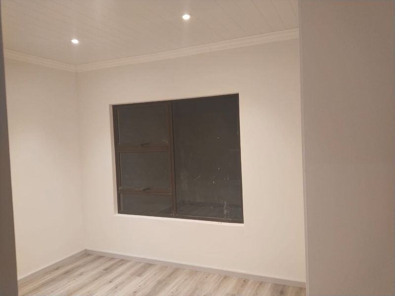 A clean, empty bedroom featuring modern laminate flooring, a tongue and groove ceiling with recessed lighting, and a dark aluminium window frame.