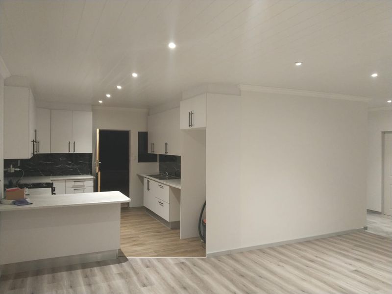 A modern, renovated kitchen featuring white cabinetry, stone countertops, dark marble-effect backsplash, and recessed lighting, seamlessly integrated into an open-plan living space.