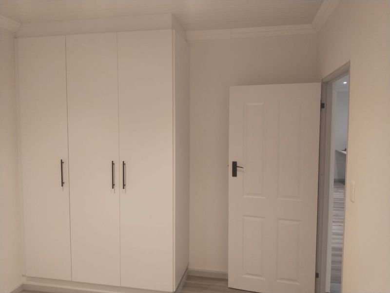 A clean, neutral bedroom featuring modern white built-in cupboards and a classic panel door, offering a bright and versatile living space.