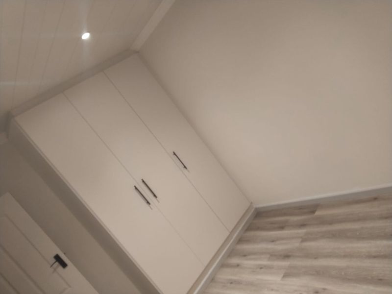 A clean, empty bedroom featuring modern laminate flooring, built-in cupboards, and a tongue and groove ceiling with recessed lighting.