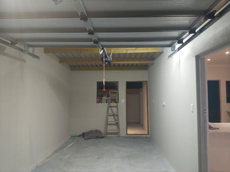 A clean, empty garage space featuring a sectional door, exposed timber ceiling joists, and a concrete floor with direct internal access.