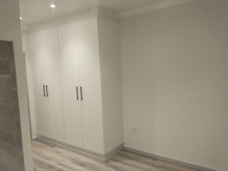 A clean, modern bedroom space featuring neutral walls, light laminate flooring, and ample built-in cupboard storage with contemporary hardware.