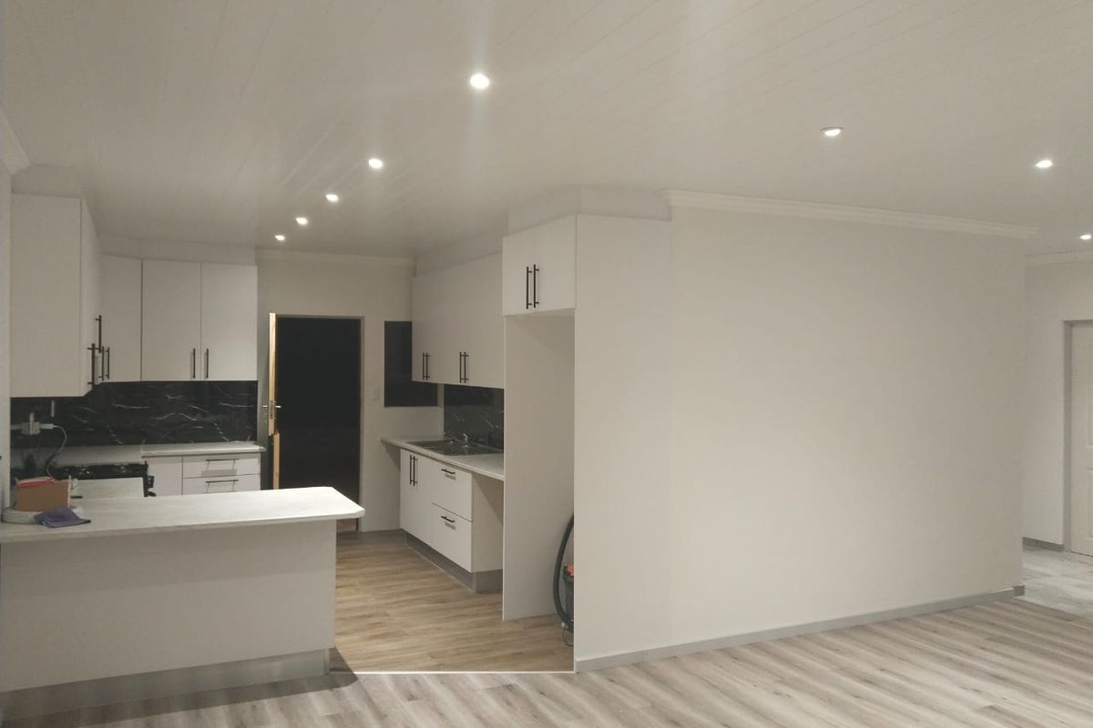A modern, renovated kitchen featuring white cabinetry, stone countertops, dark marble-effect backsplash, and recessed lighting, seamlessly integrated into an open-plan living space.