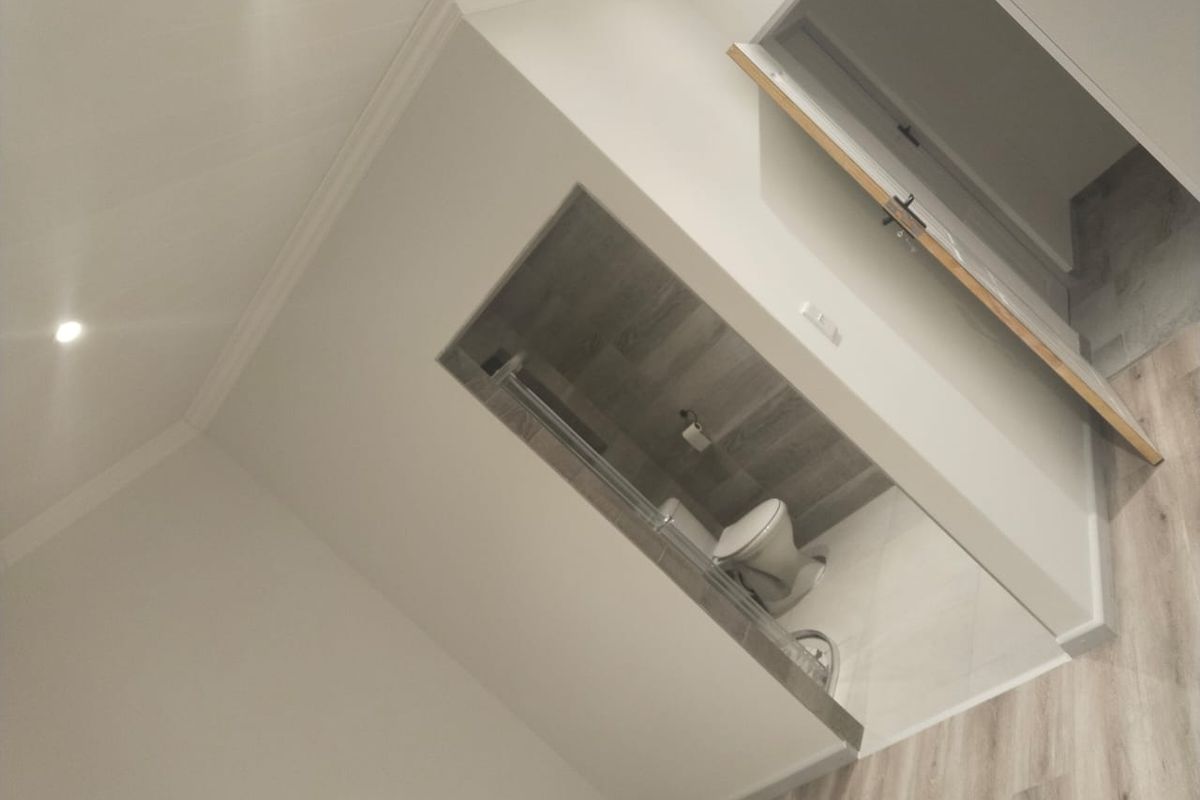 A modern, neutral-toned bathroom featuring a shower enclosure, toilet, and contemporary tiled finishes, presented in a clean, minimalist style.
