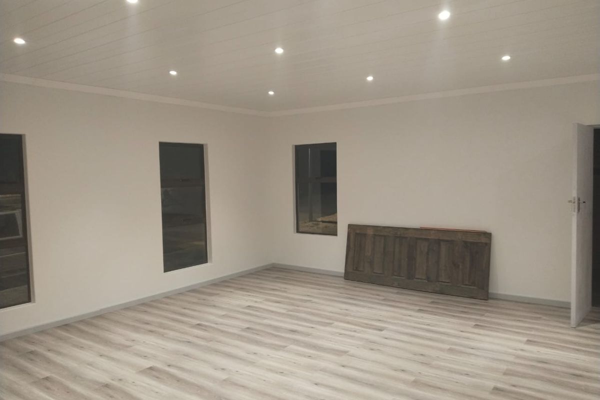 A bright, empty living area featuring modern laminate flooring, recessed downlighting, and a clean, neutral aesthetic ready for furnishing.