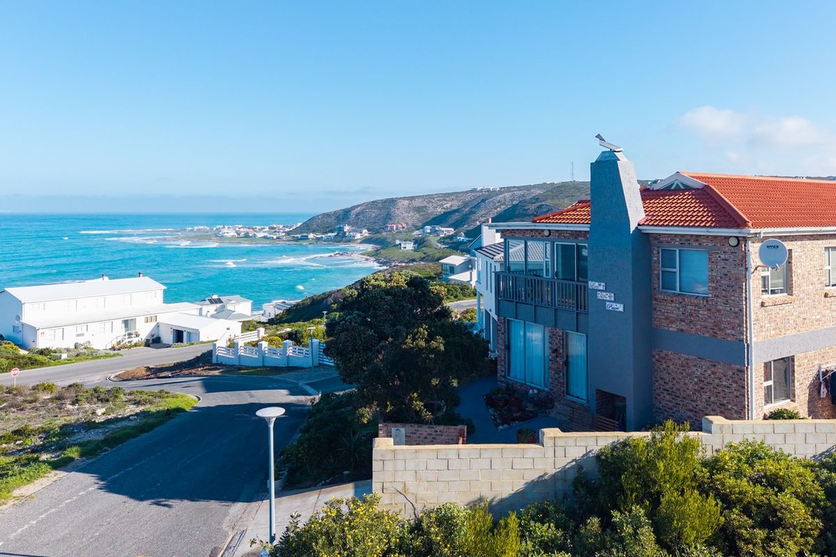 Aerial view of a coastal property featuring a brick facade, terracotta roof, and balcony with scenic ocean views.