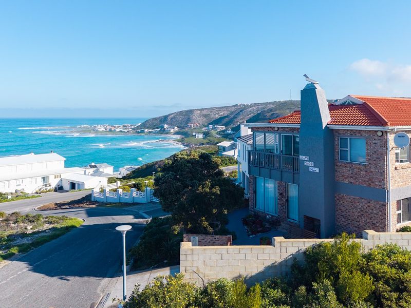 Aerial view of a coastal property featuring a brick facade, terracotta roof, and balcony with scenic ocean views.