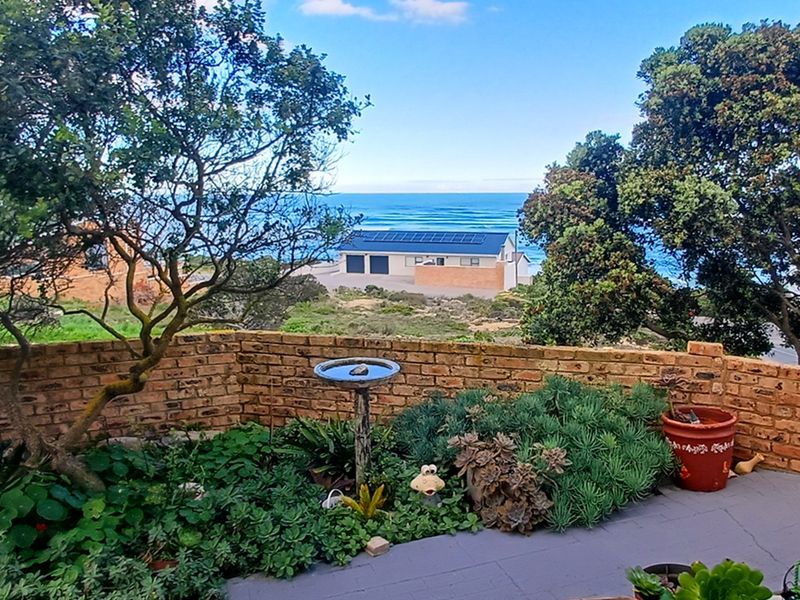 A rear garden area featuring a brick boundary wall, paved patio, and established landscaping with a scenic coastal view in the background.
