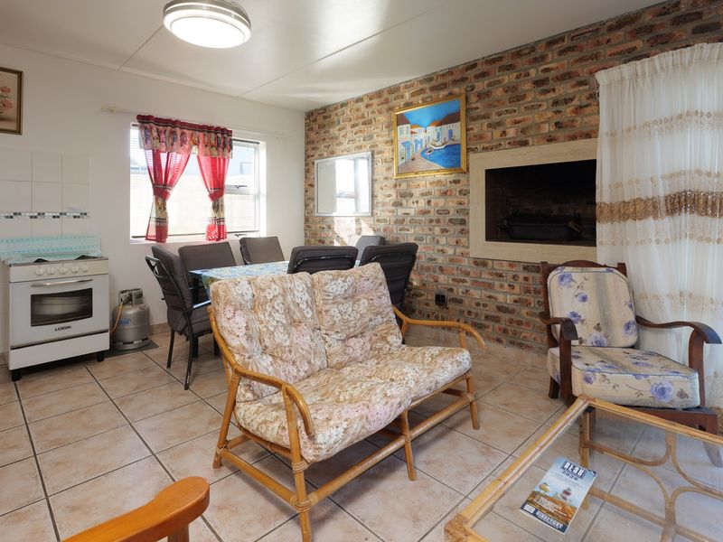 Open-plan living and kitchen area featuring tiled floors, an exposed brick wall with a built-in fireplace, and direct access to the outdoor space.