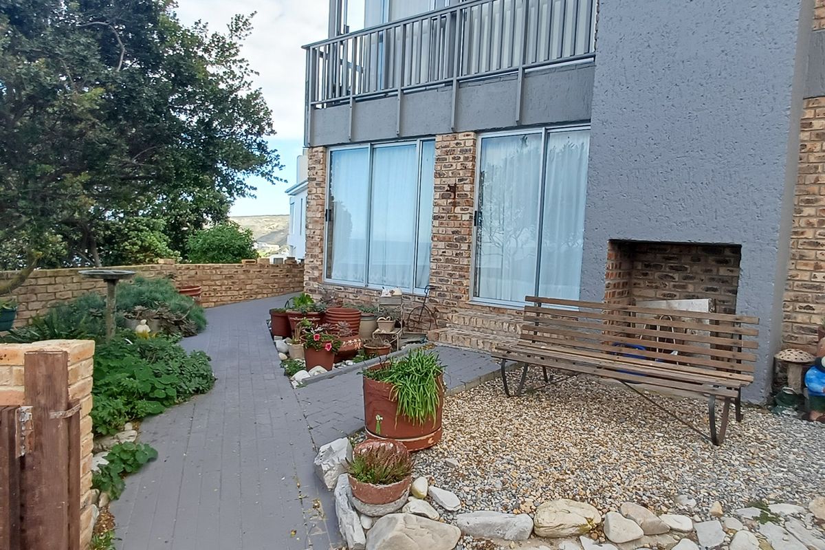 Rear exterior view of the property featuring a brick facade, paved walkway, built-in fireplace, and access to a balcony via sliding glass doors.