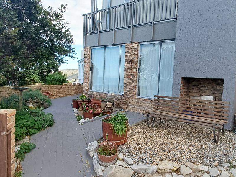 Rear exterior view of the property featuring a brick facade, paved walkway, built-in fireplace, and access to a balcony via sliding glass doors.