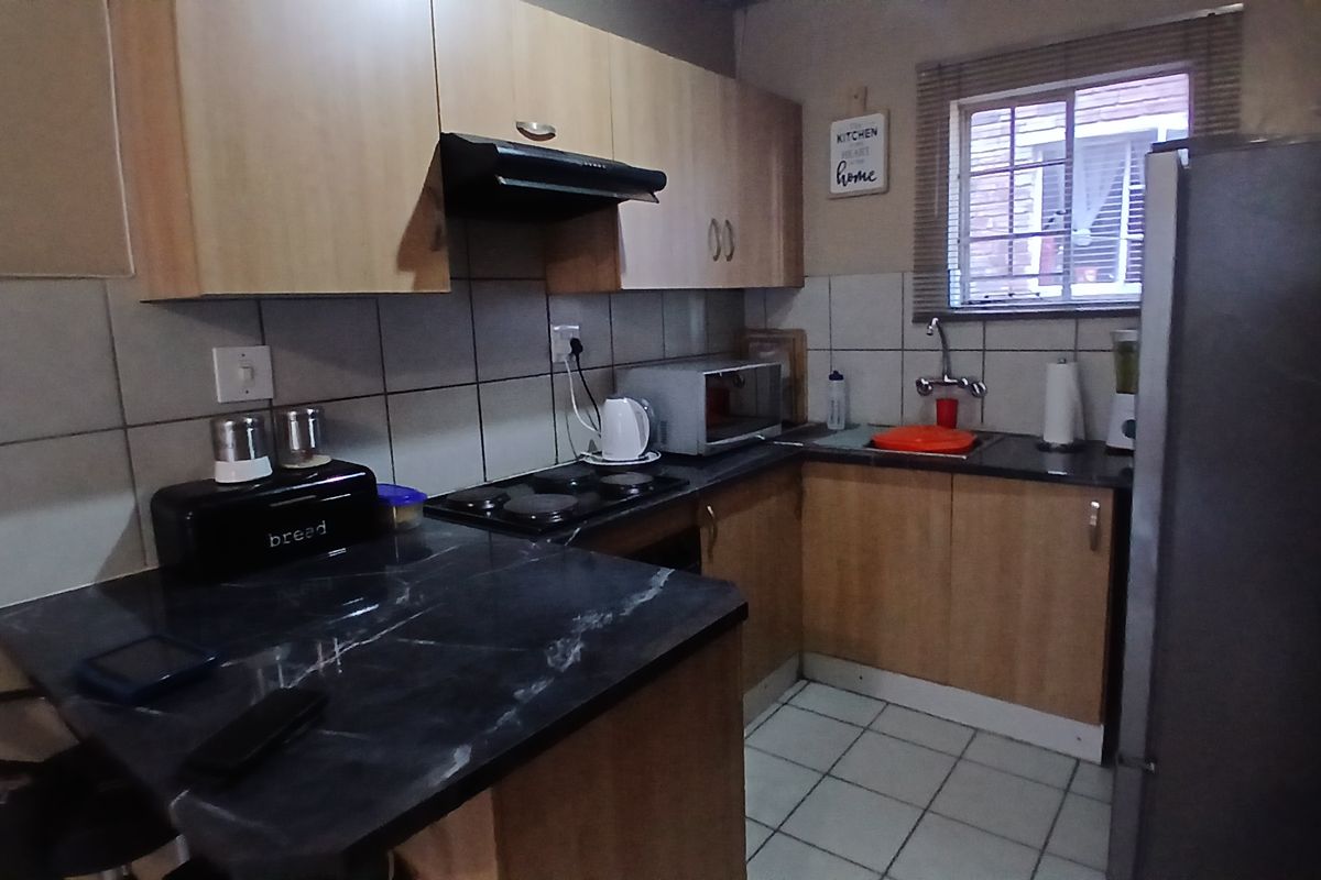 Compact kitchen featuring laminate cabinetry, dark countertops, electric hob with extractor fan, and tiled backsplash, offering a functional workspace.