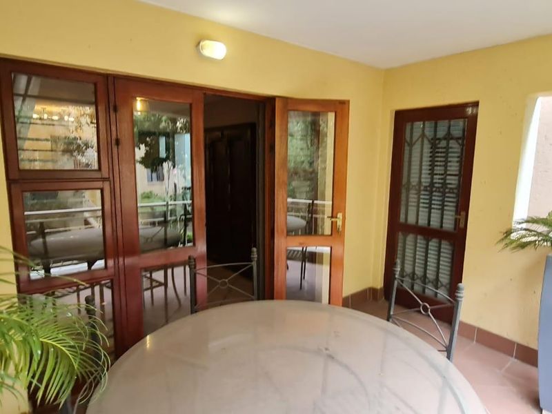 A covered patio area featuring tiled flooring, timber-framed glass doors, and a security gate, providing a functional outdoor transition space.