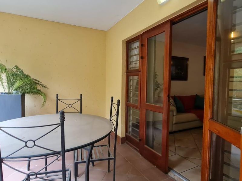 A covered patio area featuring terracotta floor tiles and wooden framed glass sliding doors providing access to the interior living space.