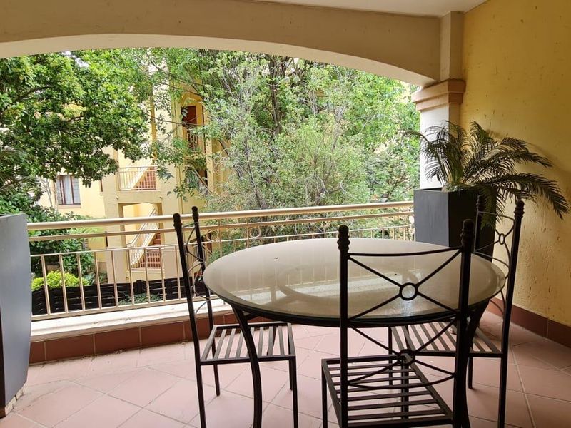 A covered balcony featuring tiled flooring, a metal balustrade, and an arched ceiling, offering a pleasant outdoor space with views of the surrounding greenery.