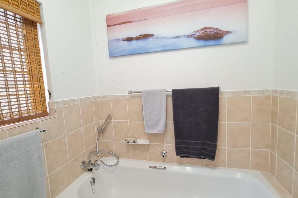 A clean bathroom featuring a white bathtub with a handheld shower mixer and neutral-toned wall tiling.