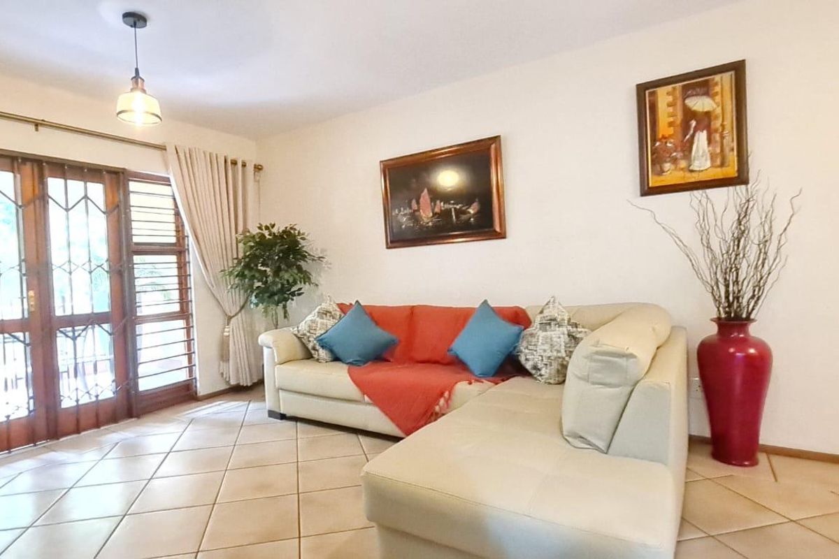 A bright living room featuring tiled flooring and a timber-framed glass door with an integrated security gate, providing access to the exterior.