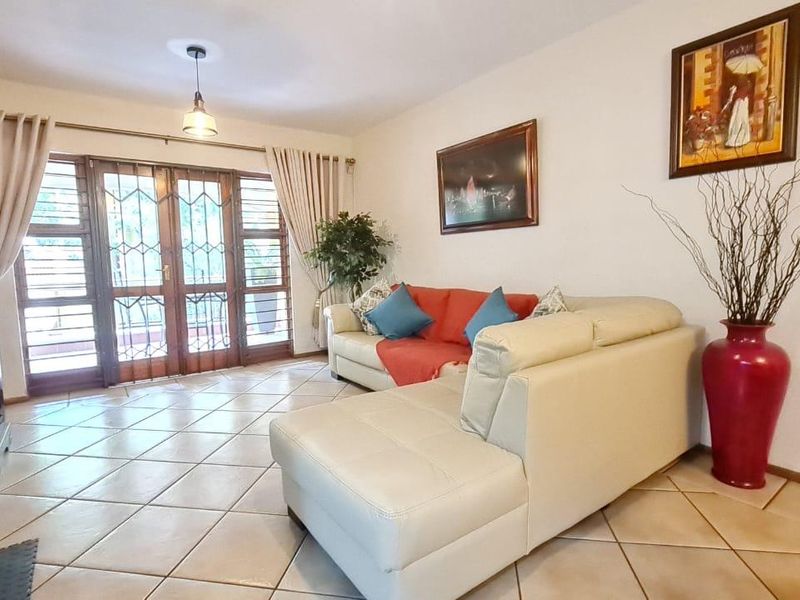 A spacious living room featuring neutral tiled flooring and double glass doors leading to an outdoor area, providing natural light and access.
