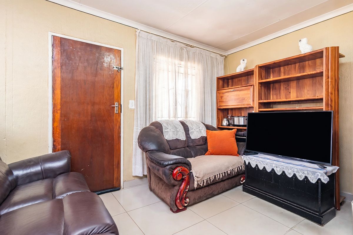 A living room featuring tiled flooring, a timber door, and coved ceilings, offering a functional space with potential for cosmetic updates.