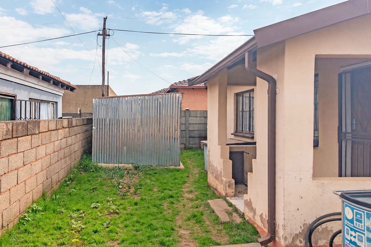 Rear exterior view of the property featuring a small garden area, a corrugated iron storage shed, and a precast concrete boundary wall.