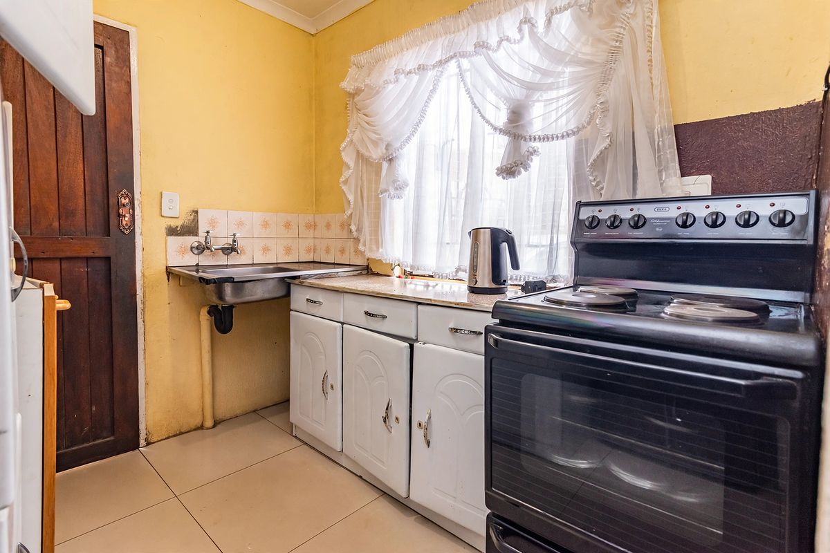 A functional kitchen featuring tiled flooring, a stainless steel sink, built-in cabinetry, and a freestanding stove with a tiled backsplash.