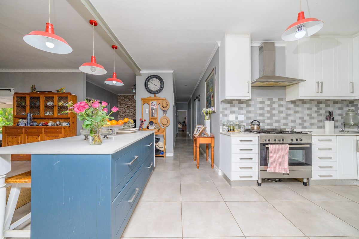 A functional kitchen featuring a central island, gas stove with extractor fan, tiled backsplash, and ample built-in cabinetry with modern pendant lighting.