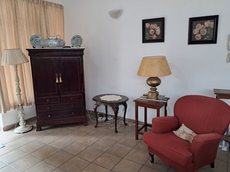 A living room area featuring ceramic floor tiles and a wall-mounted light fixture, offering a functional space ready for modernization.