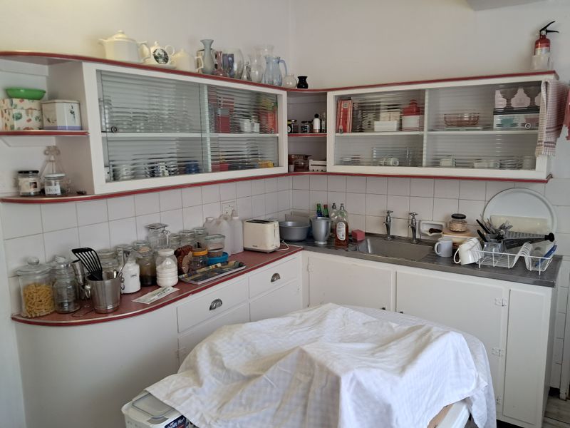 A dated kitchen featuring original built-in cabinetry with sliding glass doors, a stainless steel sink, and tiled backsplash, offering potential for modern renovation.