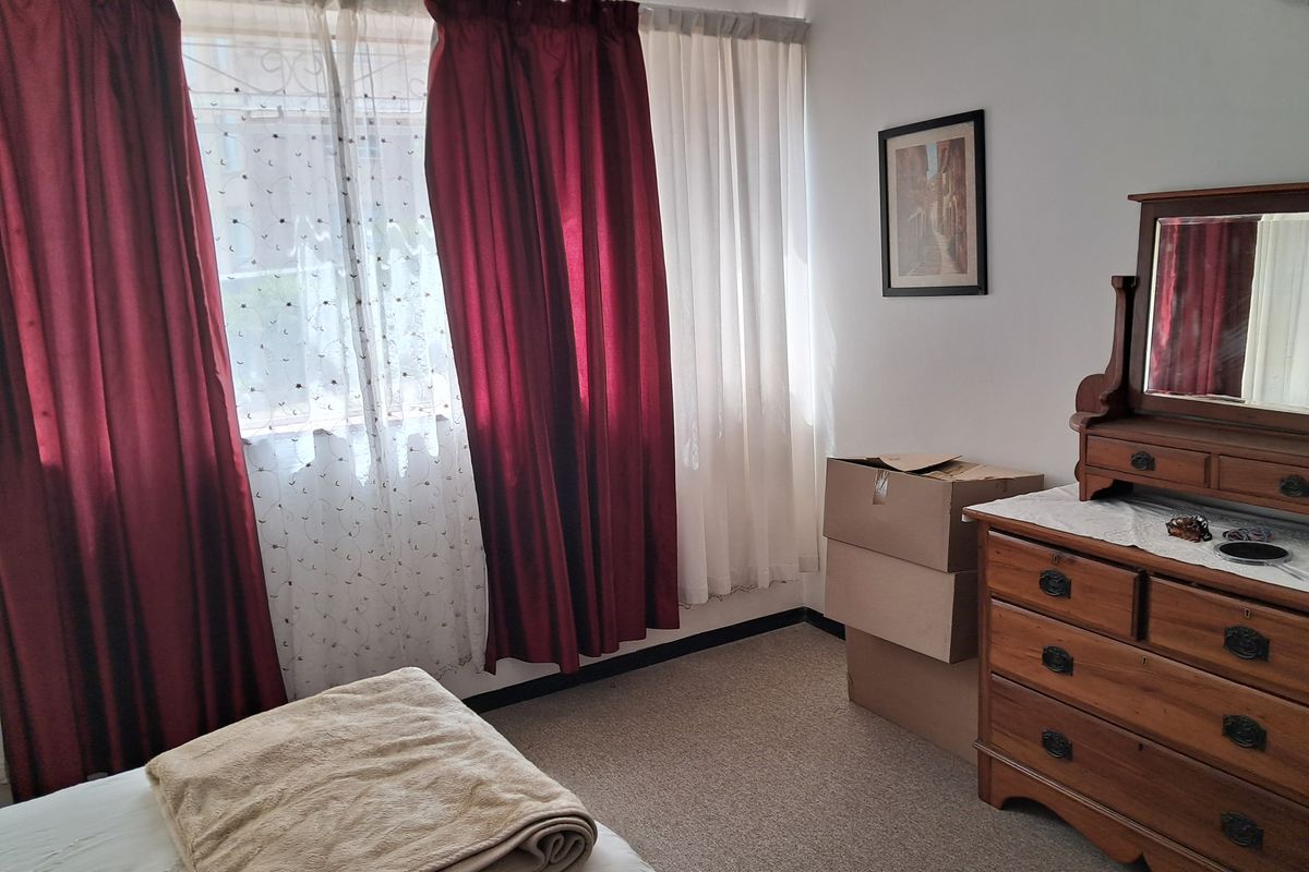 A standard bedroom featuring carpeted flooring and window security bars, offering a functional space with natural light.