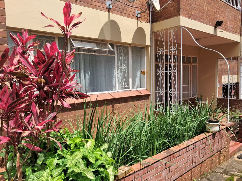 Front exterior view of the apartment featuring a brick facade, security gates, and a built-in brick planter box with established garden beds.