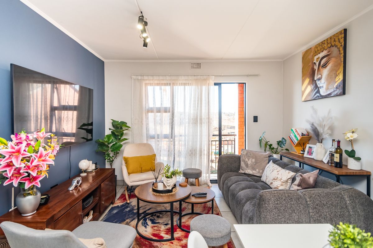 A well-maintained living room featuring a bold blue accent wall, modern track lighting, and a sliding glass door leading to an outdoor balcony.