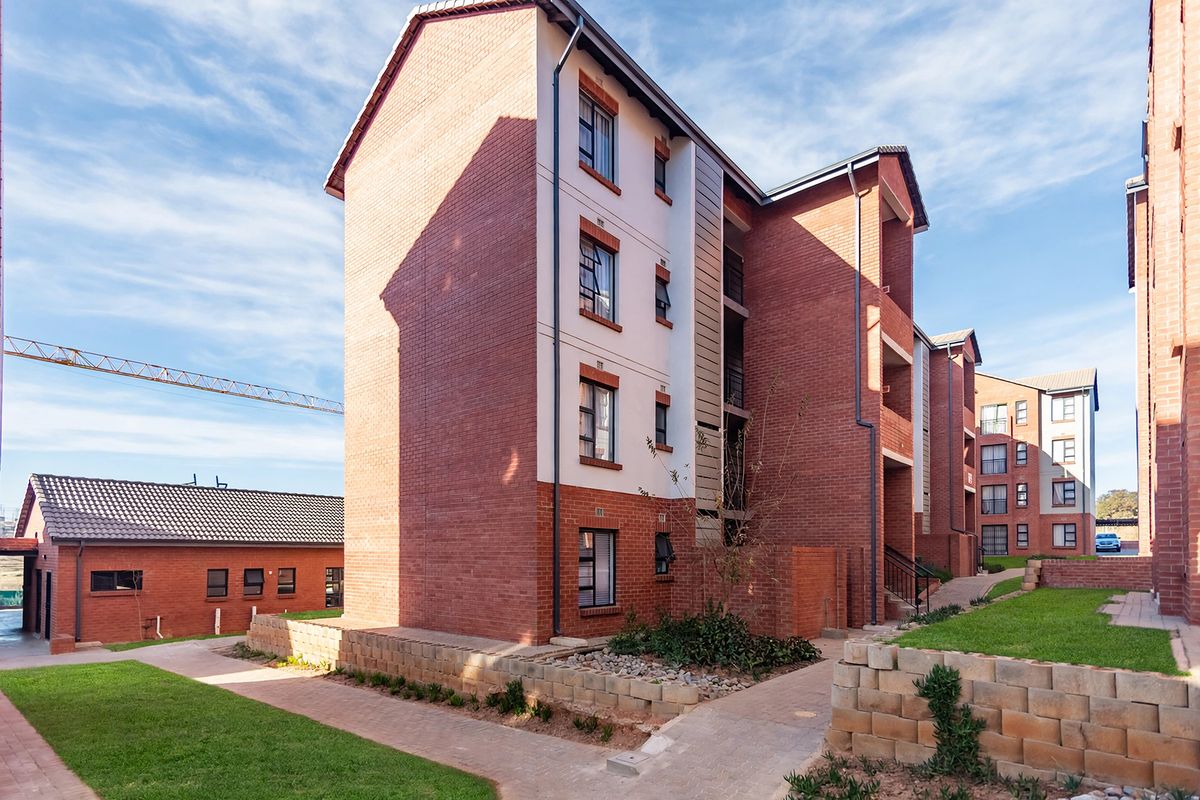 A view of the townhouse complex exterior featuring face brick construction, paved walkways, and well-maintained communal garden areas.