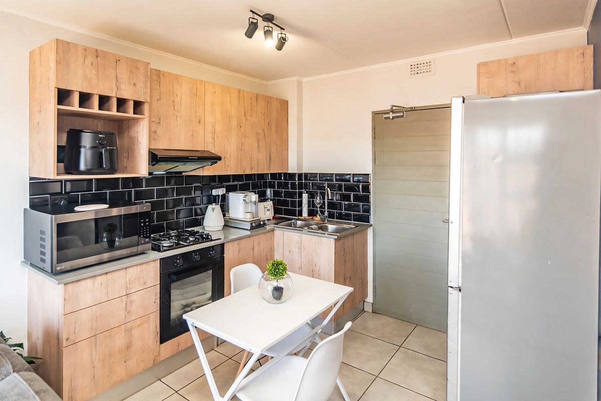 Modern kitchen featuring wood-look cabinetry, black subway tile splashback, gas hob, electric oven, and tiled flooring with an integrated dining area.