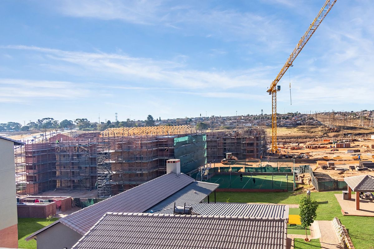 Aerial view of a residential development under construction, featuring ongoing building works, a tower crane, and established communal sports facilities.