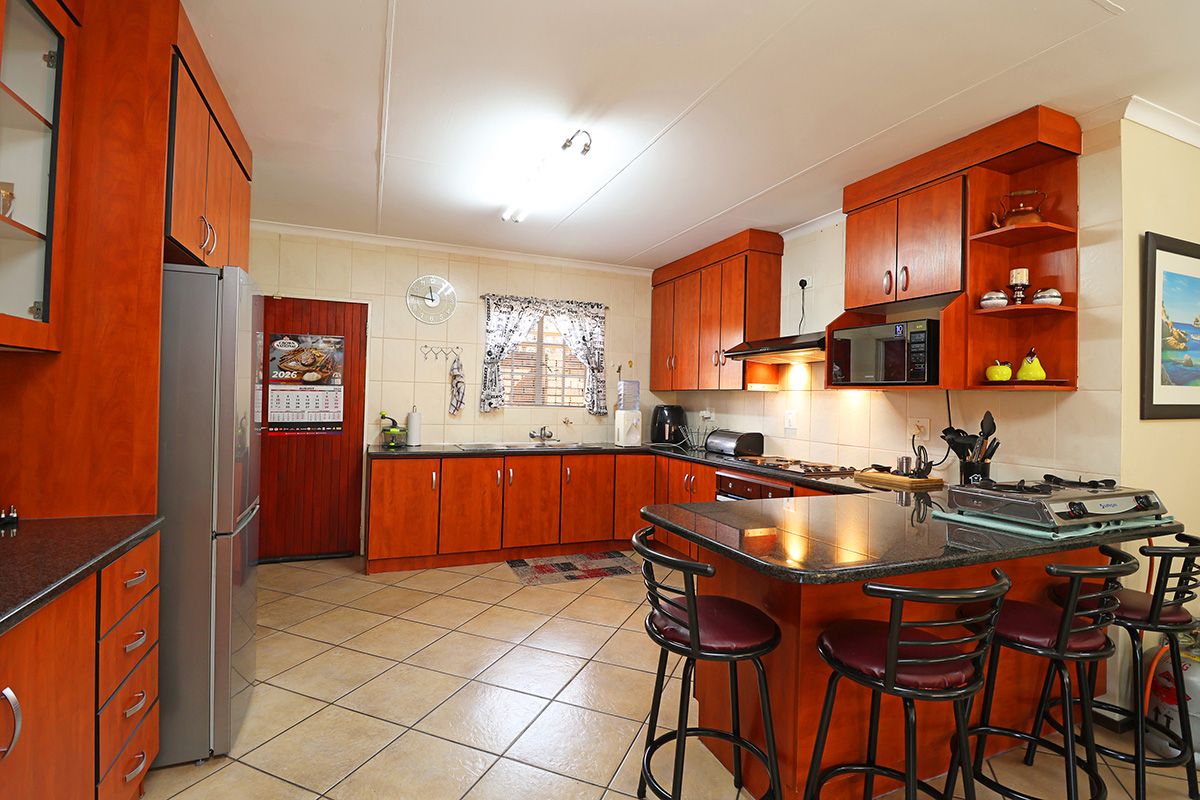 A functional kitchen featuring warm-toned wooden cabinetry, granite countertops, a breakfast nook, and tiled flooring, offering a practical layout for daily cooking.
