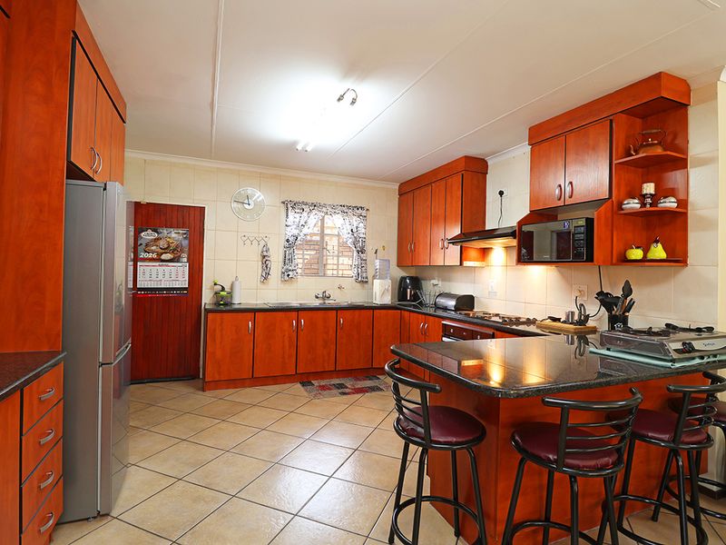 A functional kitchen featuring warm-toned wooden cabinetry, granite countertops, a breakfast nook, and tiled flooring, offering a practical layout for daily cooking.