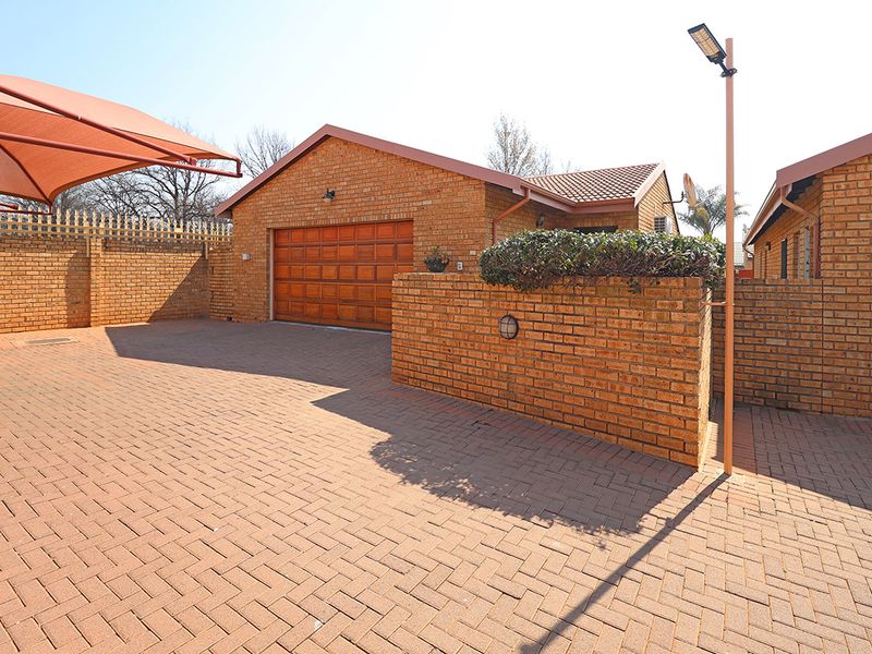 Front exterior view featuring a facebrick facade, paved driveway, wooden garage door, and a shade sail structure.