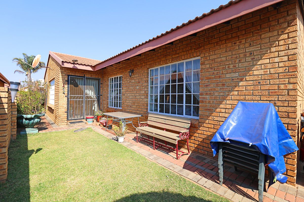 A rear view of the house featuring a face brick facade, tiled roof, paved patio area, and a small private lawn.
