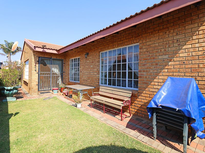 A rear view of the house featuring a face brick facade, tiled roof, paved patio area, and a small private lawn.
