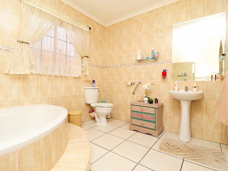 A functional bathroom featuring a built-in bathtub, pedestal basin, and toilet, finished with neutral wall and floor tiling throughout.