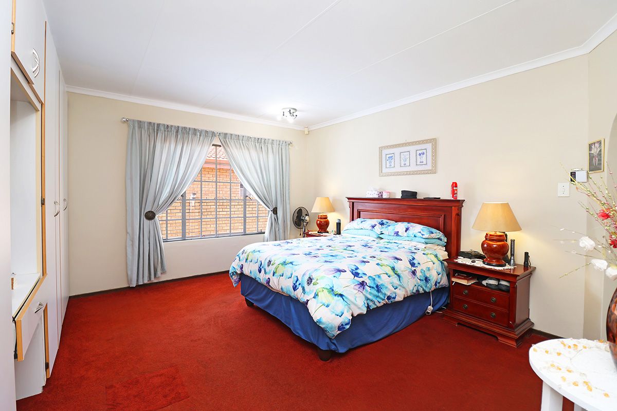 A spacious bedroom featuring built-in cupboards, carpeted flooring, and a window with security bars.