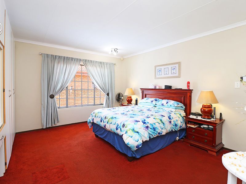 A spacious bedroom featuring built-in cupboards, carpeted flooring, and a window with security bars.